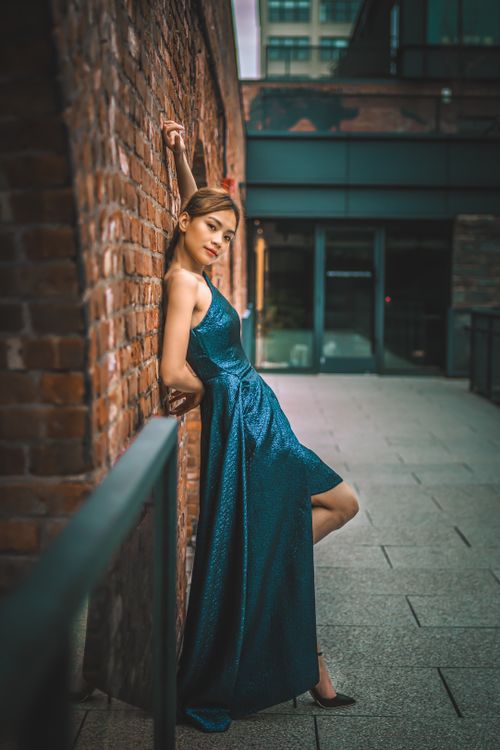 Free Side view of gorgeous young Asian female in green long dress leaning on brick wall Stock Photo