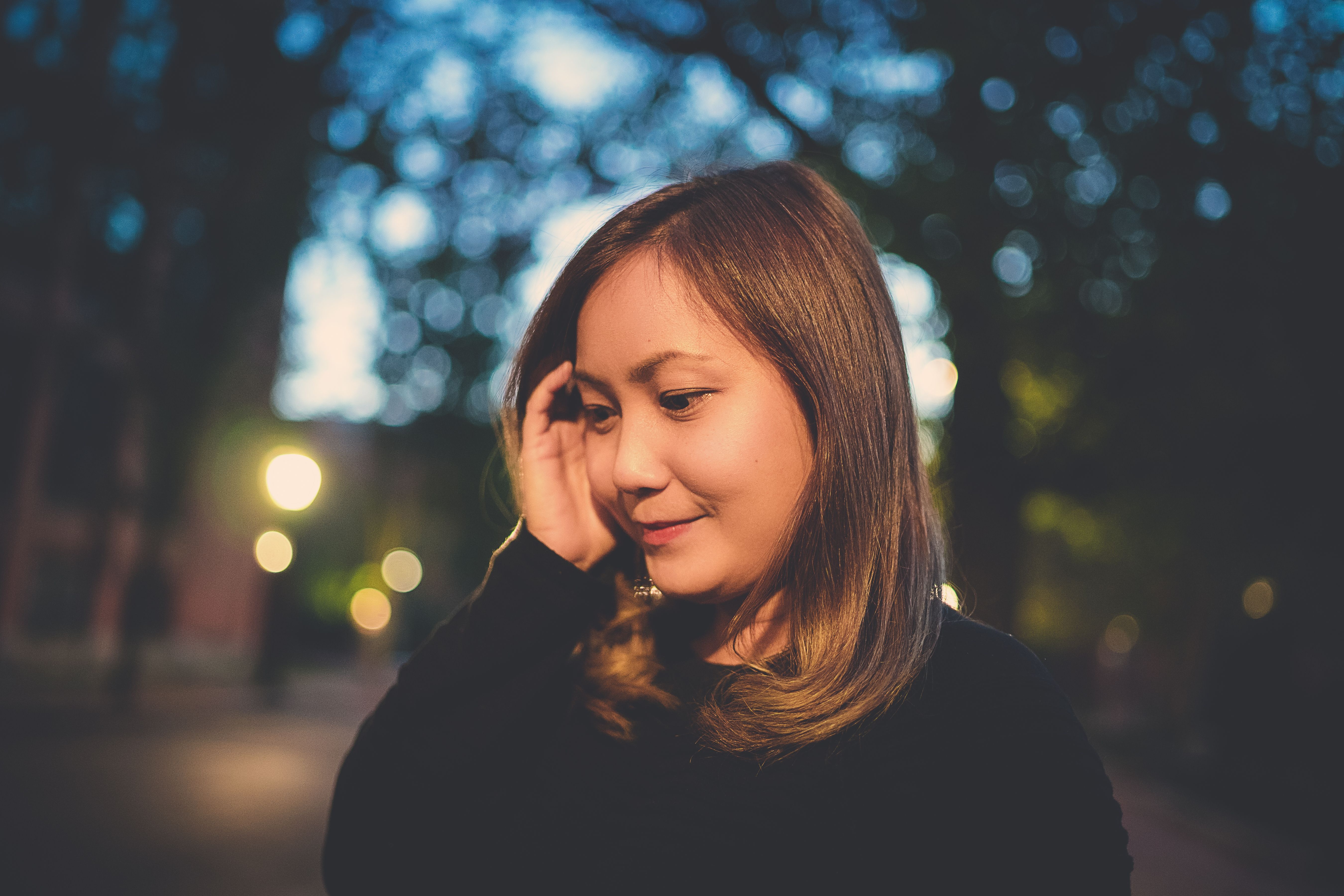 晚上，一位平静的亚洲女人穿着休闲装，若有所思地抚摸着头发，目光望向街上的别处