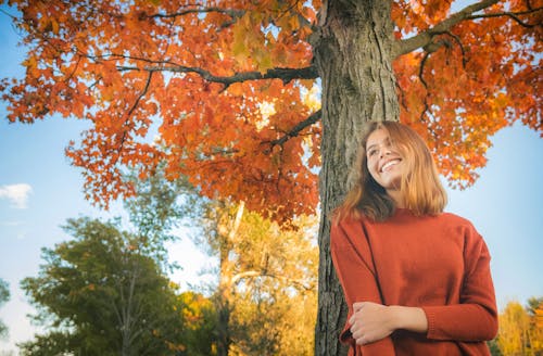 Free Cheerful female leaning on autumn tree in park Stock Photo