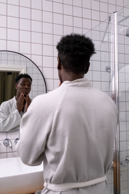 Free An adult man in a white bathrobe examines his face in a modern bathroom mirror. Stock Photo