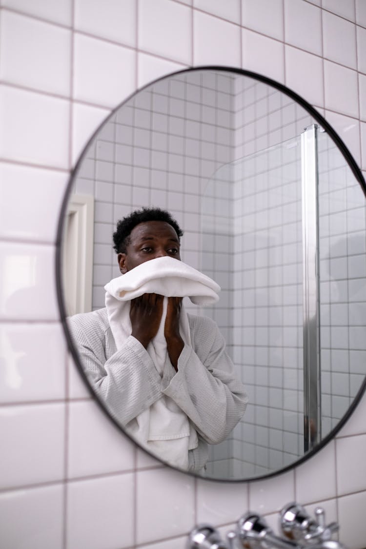 Man In White Robe Wiping His Face In Front Of A Mirror 