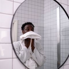 A man in a bathrobe drying his face in a bright white bathroom