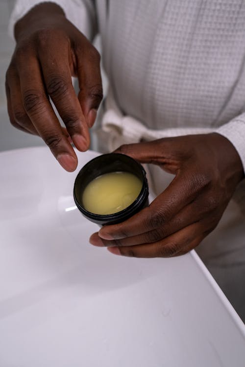 Person Holding Black Container With Yellow Cream 