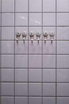 Close-up of wall hooks with the word 'REPEAT' on white tiles in a bathroom.