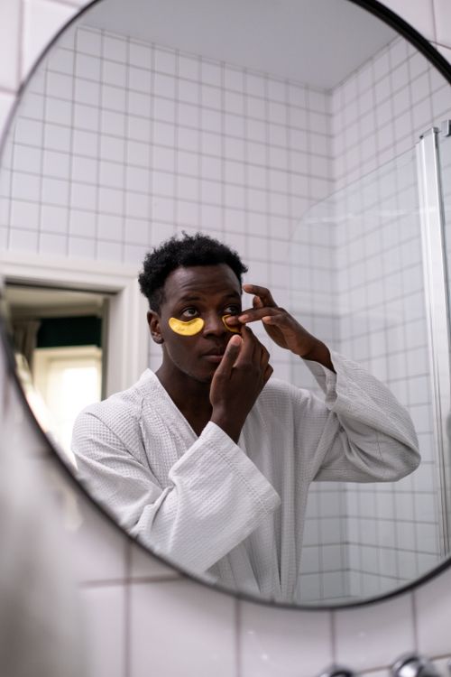 Free A man in a bathrobe applies under-eye masks while looking in the mirror. Stock Photo