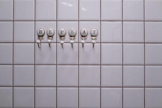 White tiled wall with towel hooks spelling 'REPEAT', showcasing a conceptual minimalist design.