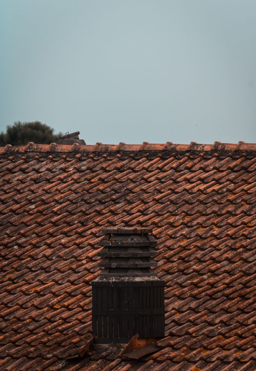 Free Close-up view of a rustic clay tile roof featuring a unique wooden chimney against a clear sky. Stock Photo