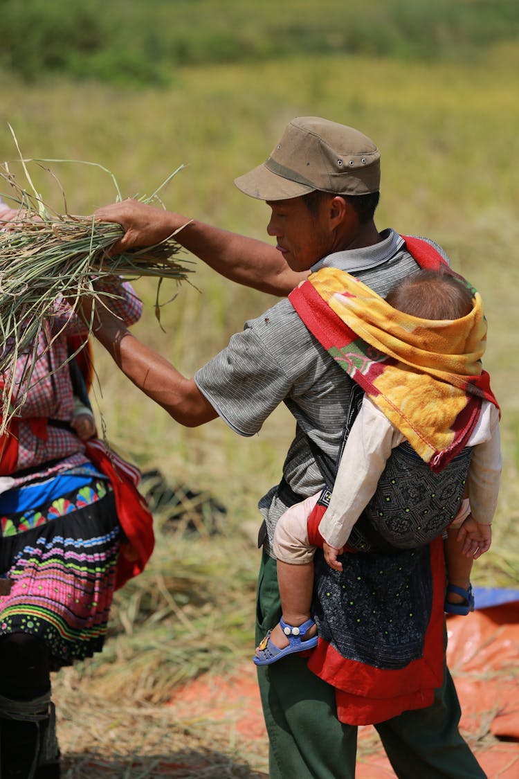 Man Working On Farm With Child On Back