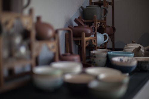 Various ceramic teapots in different shapes and traditional Asian cups placed on table in kitchen