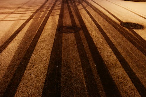 From above of manholes on snowy asphalt road with tire tracks in winter evening