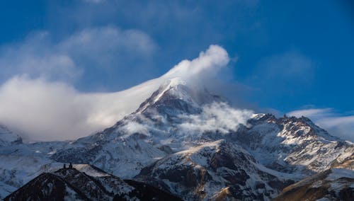 Snow Covered Mountain Surrounded by White Clouds Under Blue Sky 
