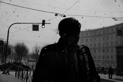 Free Black and white of anonymous male in outerwear listening to music in earphones while walking on sidewalk during snowfall Stock Photo