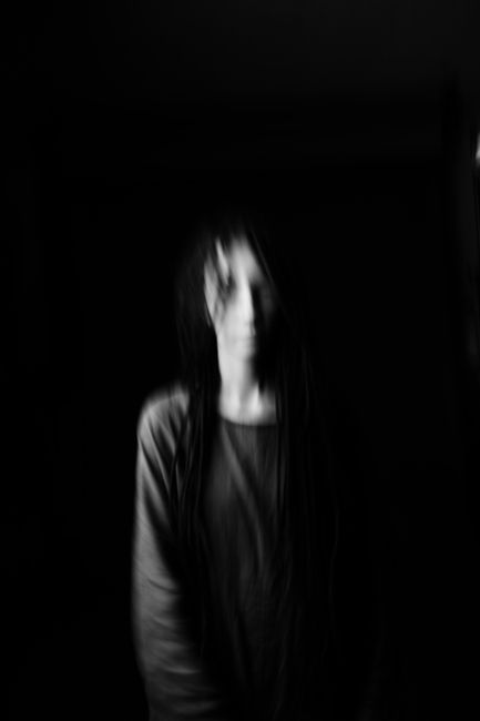 Haunting blurred portrait of a woman on a dark background, creating a ghostly effect.