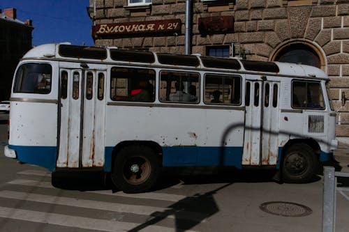 Old fashioned rusty bus with people driving on intersection at corner of city street