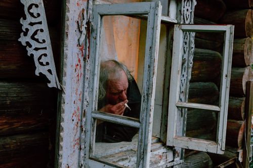 Free Senior male with gray hair smoking cigarette through opened window of shabby rural  house Stock Photo