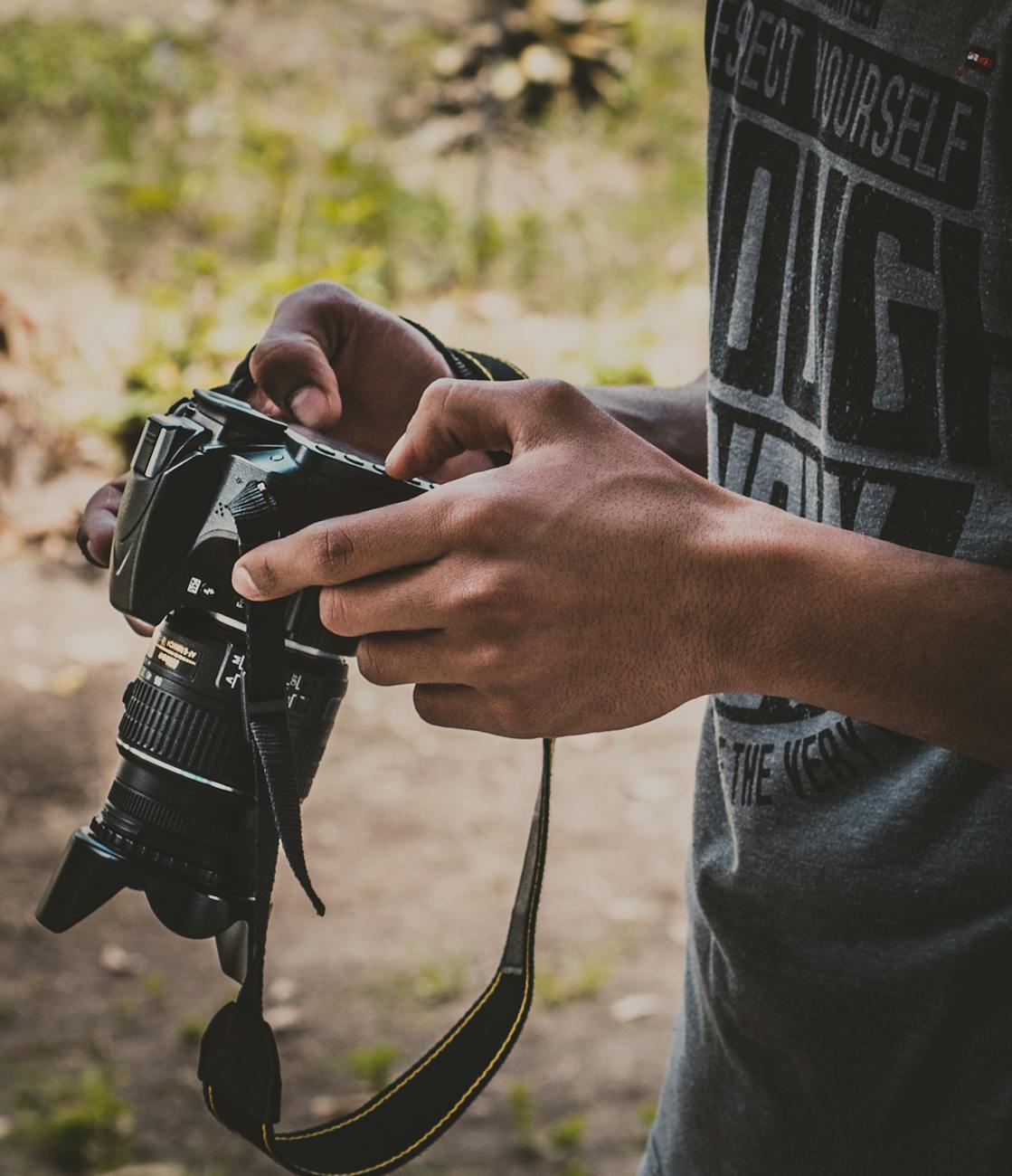 Close-up of hands holding a DSLR camera in an outdoor setting, capturing the essence of photography.