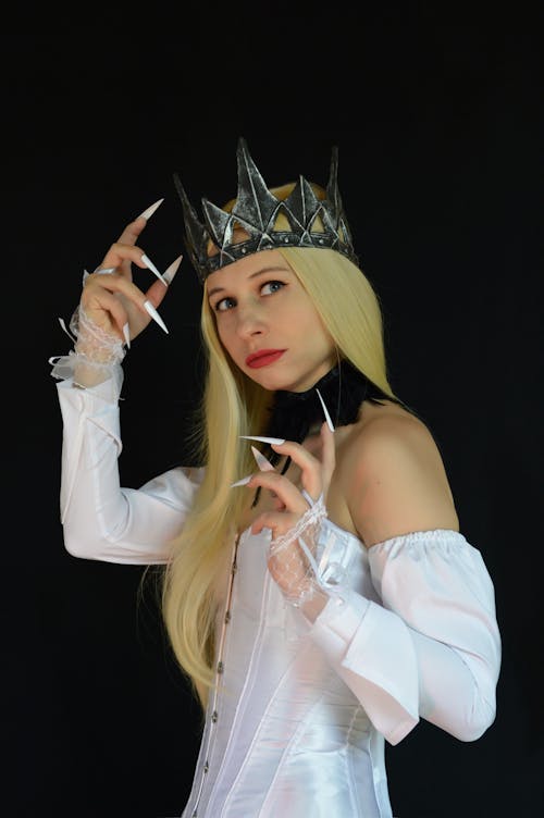 Side view of strange female in crown and fake nails wearing white corset for Halloween celebration