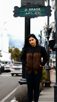 Casual portrait of a woman standing on Braga Street, Jakarta. Urban vibe with traffic and cityscape. - Fotografer Sidoarjo