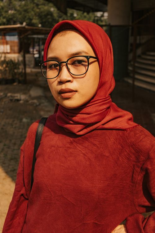Free Portrait of a woman outdoors wearing a red hijab and eyeglasses, exuding confidence. Stock Photo