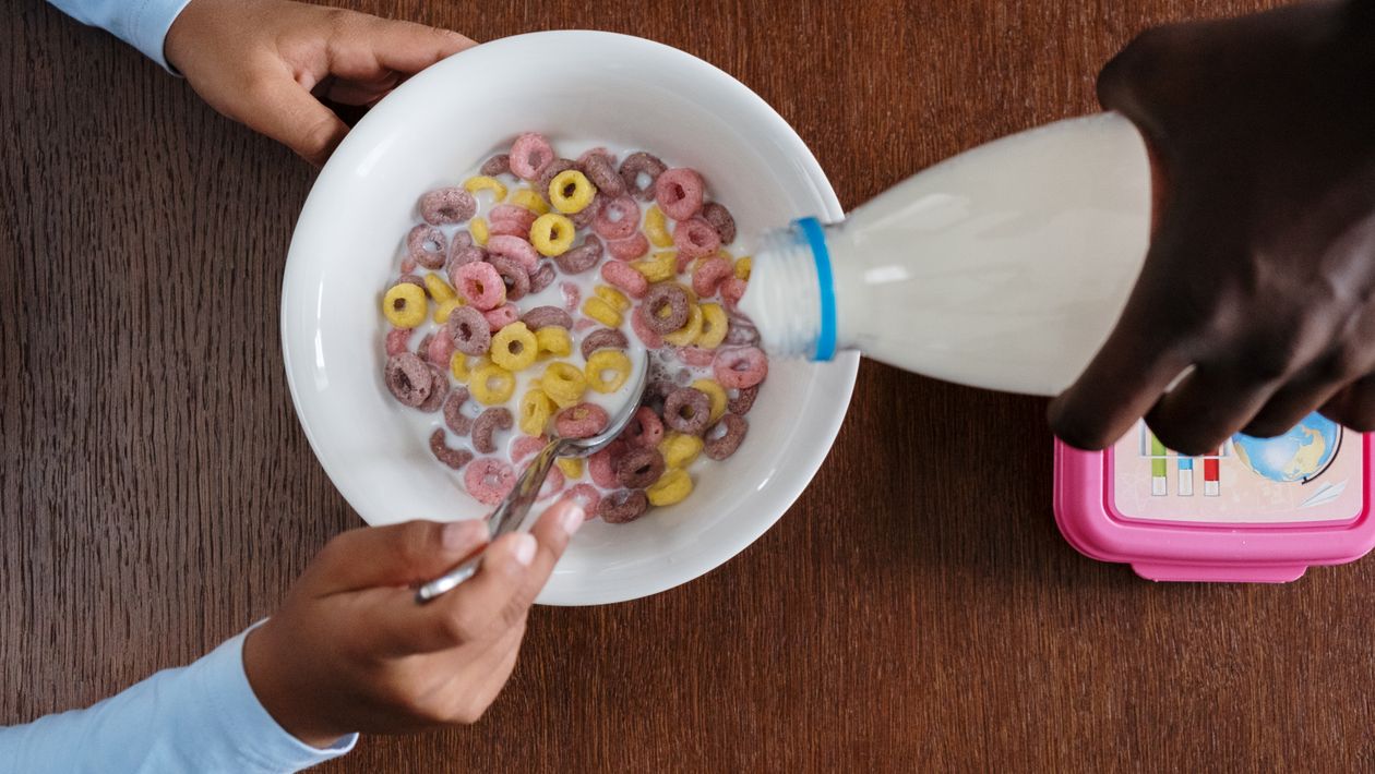 Someone pouring milk into a bowl of colorful breakfast cereal on a table.