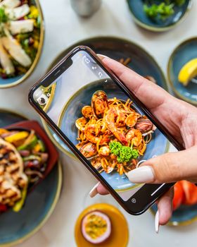 Close-up of a smartphone capturing a vibrant seafood pasta dish in a restaurant setting.