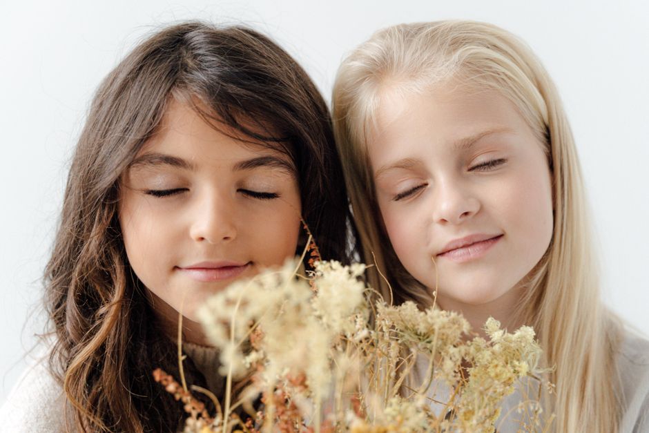Portrait of two girls with eyes closed, smiling with flowers in front of them on a white background.