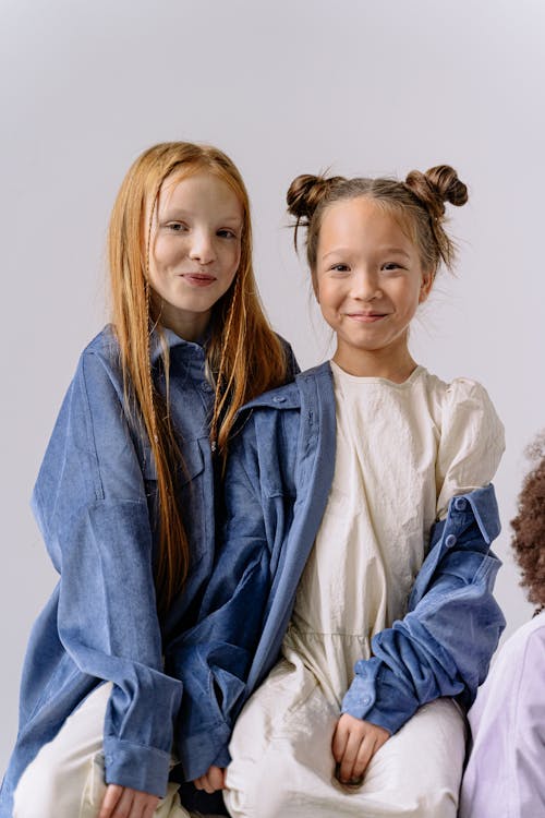 Girls Wearing White Dress Under a Blue Button Up Shirt Sitting Close Together