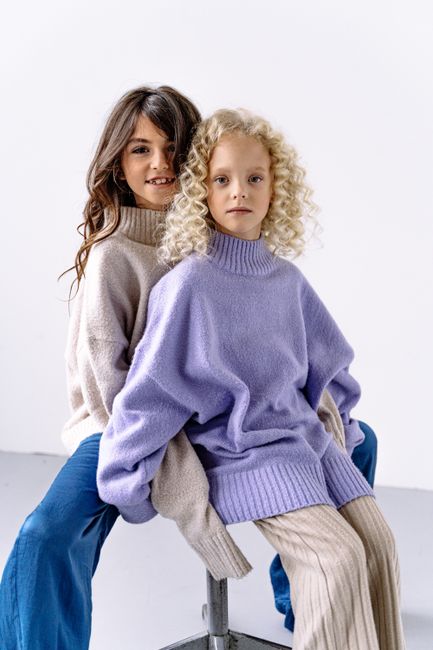 Two young girls in cozy sweaters posing in a bright studio setting.
