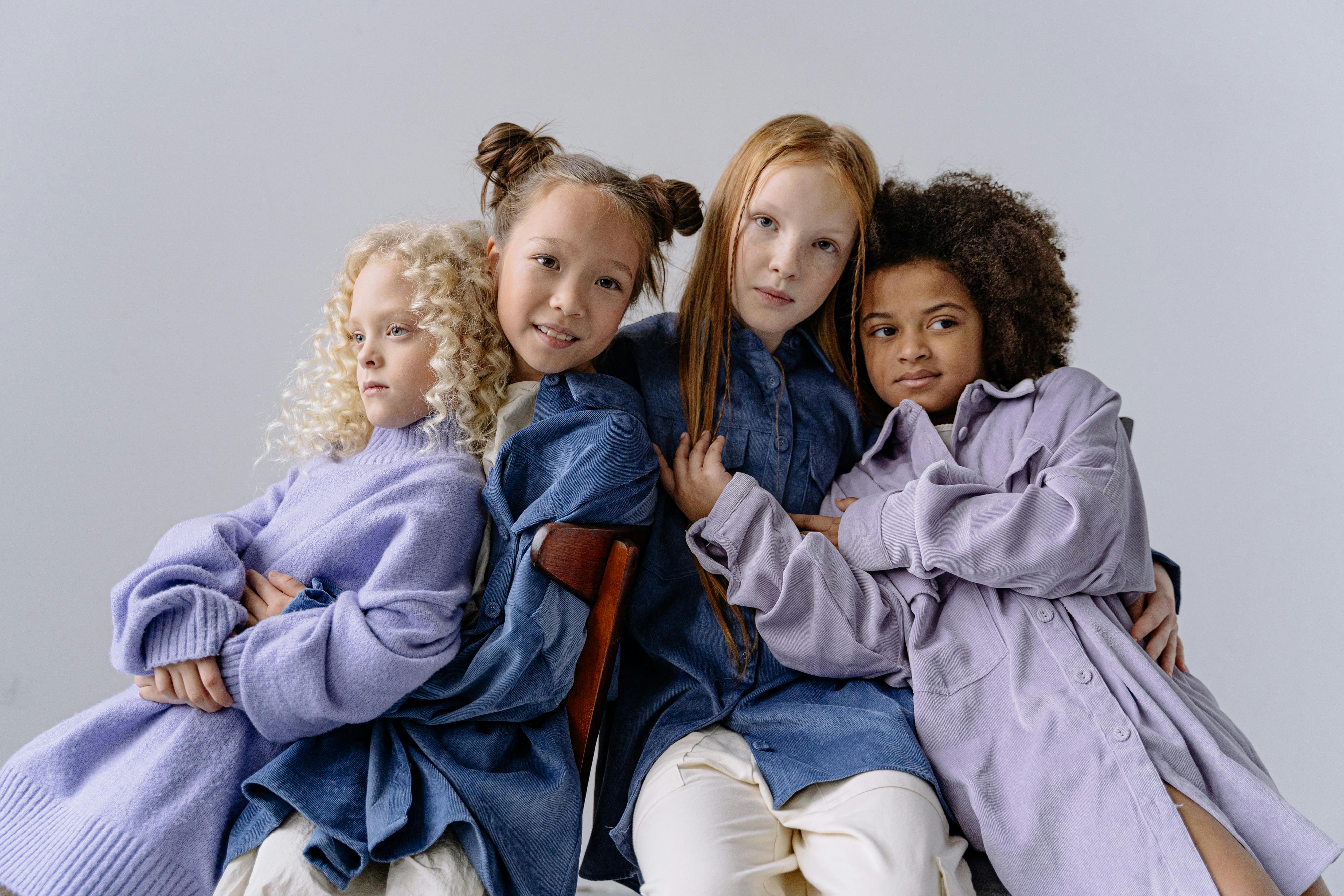 Four children in cozy clothing seated together, symbolizing unity and diversity on a white background.