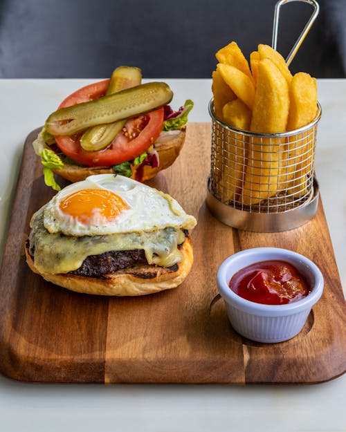 A Burger with Beef and Fried Egg and Potato Fries with Ketchup on the Side