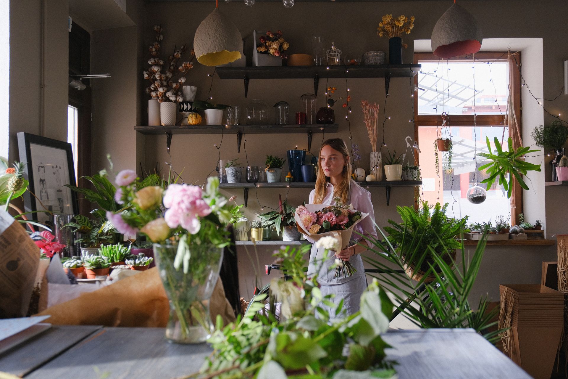 Florist in a cozy flower shop arranging a bouquet surrounded by various indoor plants.