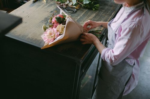 Free A florist arranges a colorful flower bouquet on a wooden table in a serene indoor setting. Stock Photo