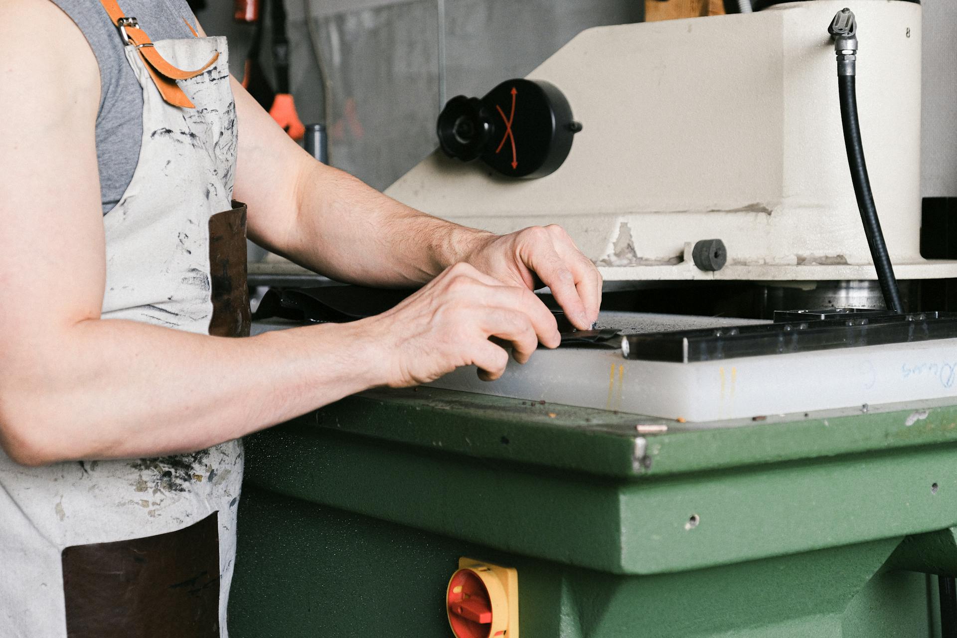 Close-up of man operating machinery in an industrial setting, wearing an apron.