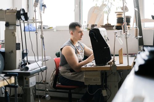 Free A man in an apron works diligently at a sewing machine in a bright workshop. Stock Photo