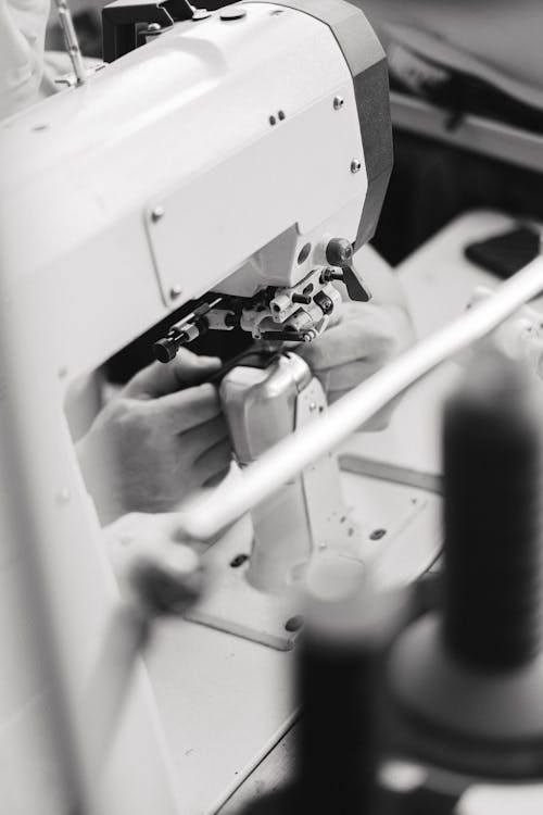 Grayscale Photo of a Person Using Industrial Sewing Machine