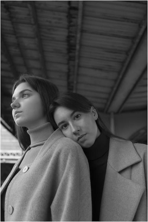 Black and white of attractive woman in coat leaning head on shoulder of partner and looking at camera