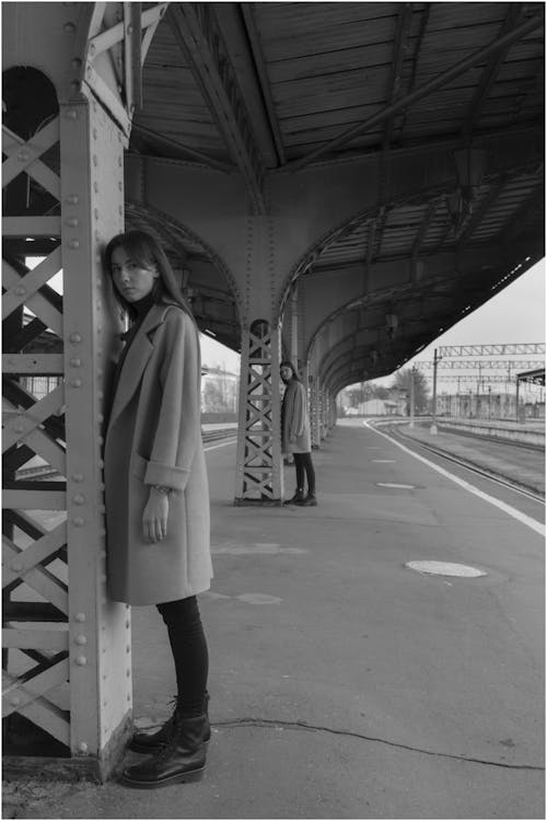 Free Full body of female models in trendy clothes standing near iron pillars on railway platform and looking at camera Stock Photo