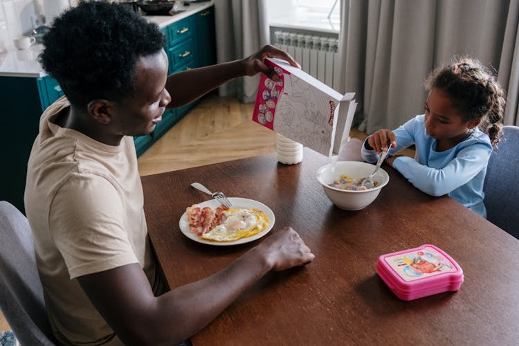 Father And Daughter Eating Breakfast On The Table