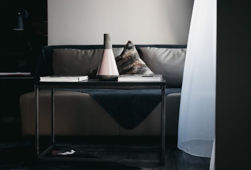 Stylish vase and books arranged on table placed near comfortable leather couch in modern apartment