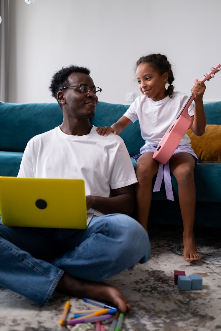 A Man Sitting On The Floor With Laptop Beside A Girl Holding Ukelele