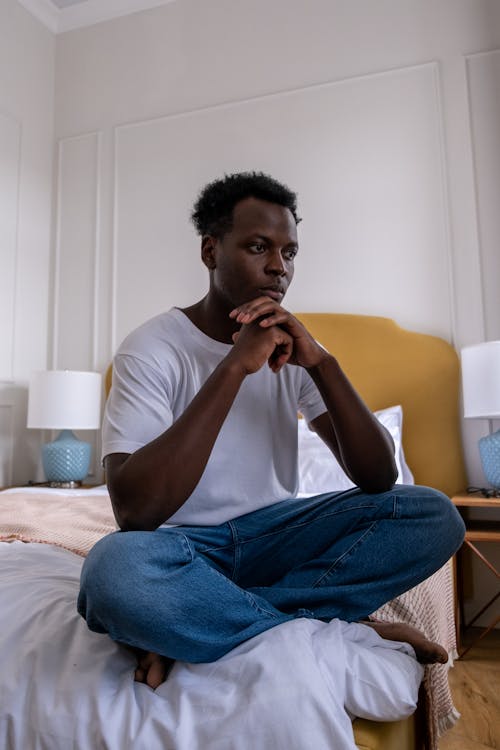 Homme En T Shirt à Col Rond Blanc Et Jeans En Denim Bleu Assis Sur Un Lit Blanc