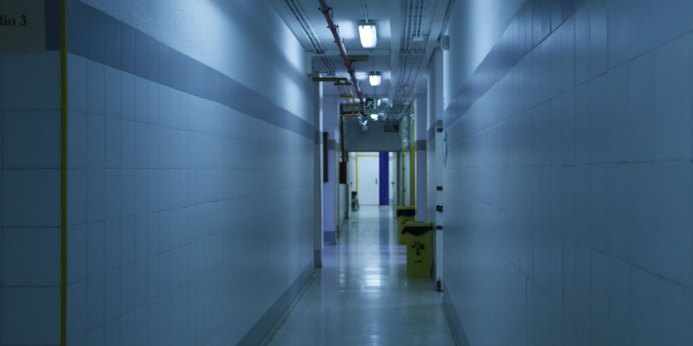 A deserted, dimly lit hallway with tiled walls and overhead lights.