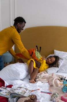 父女俩躺在床上，周围散落着玩具和书籍，一起享受玩耍的时光