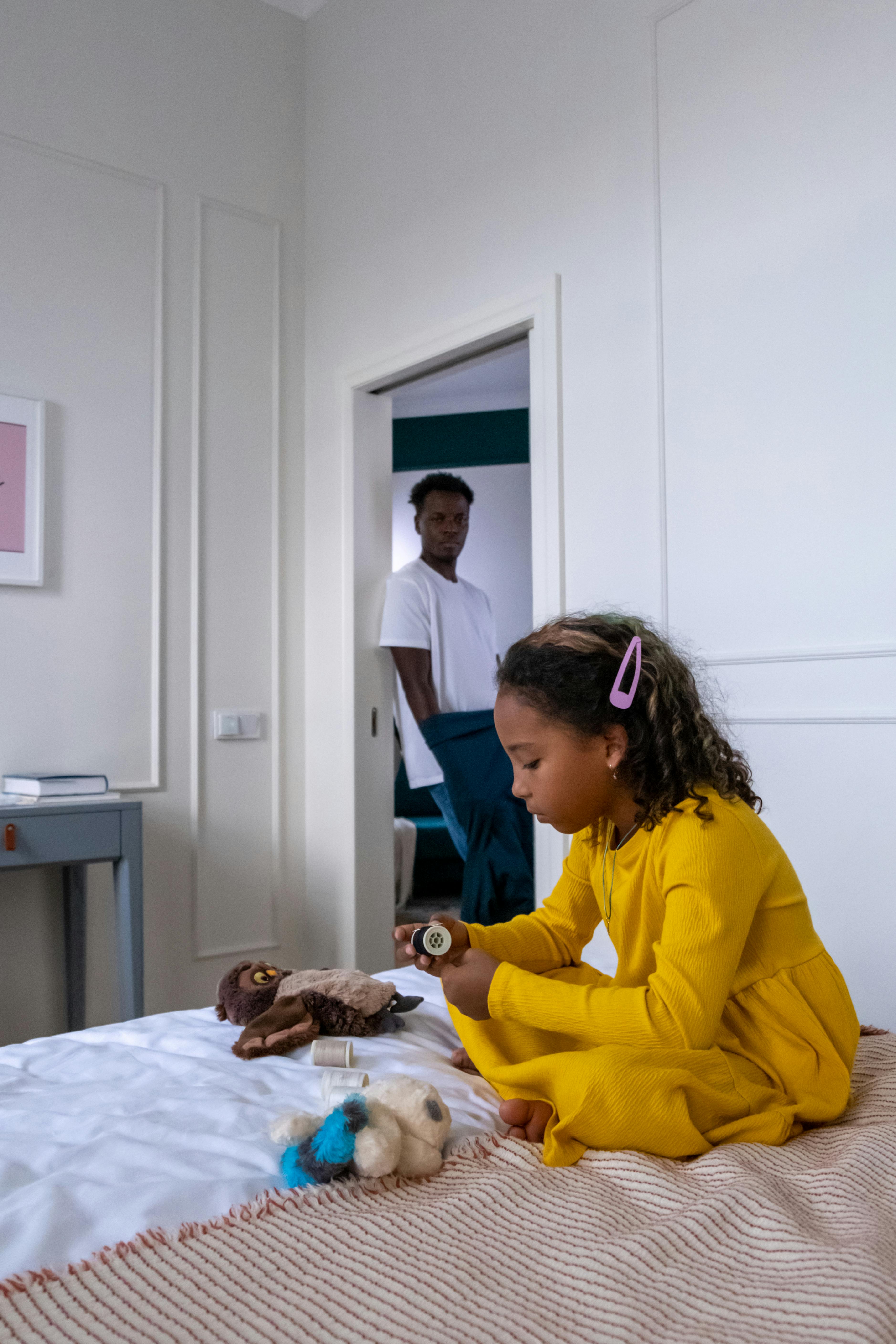 a man standing on a bedroom doorway looking at a girl sitting on bed