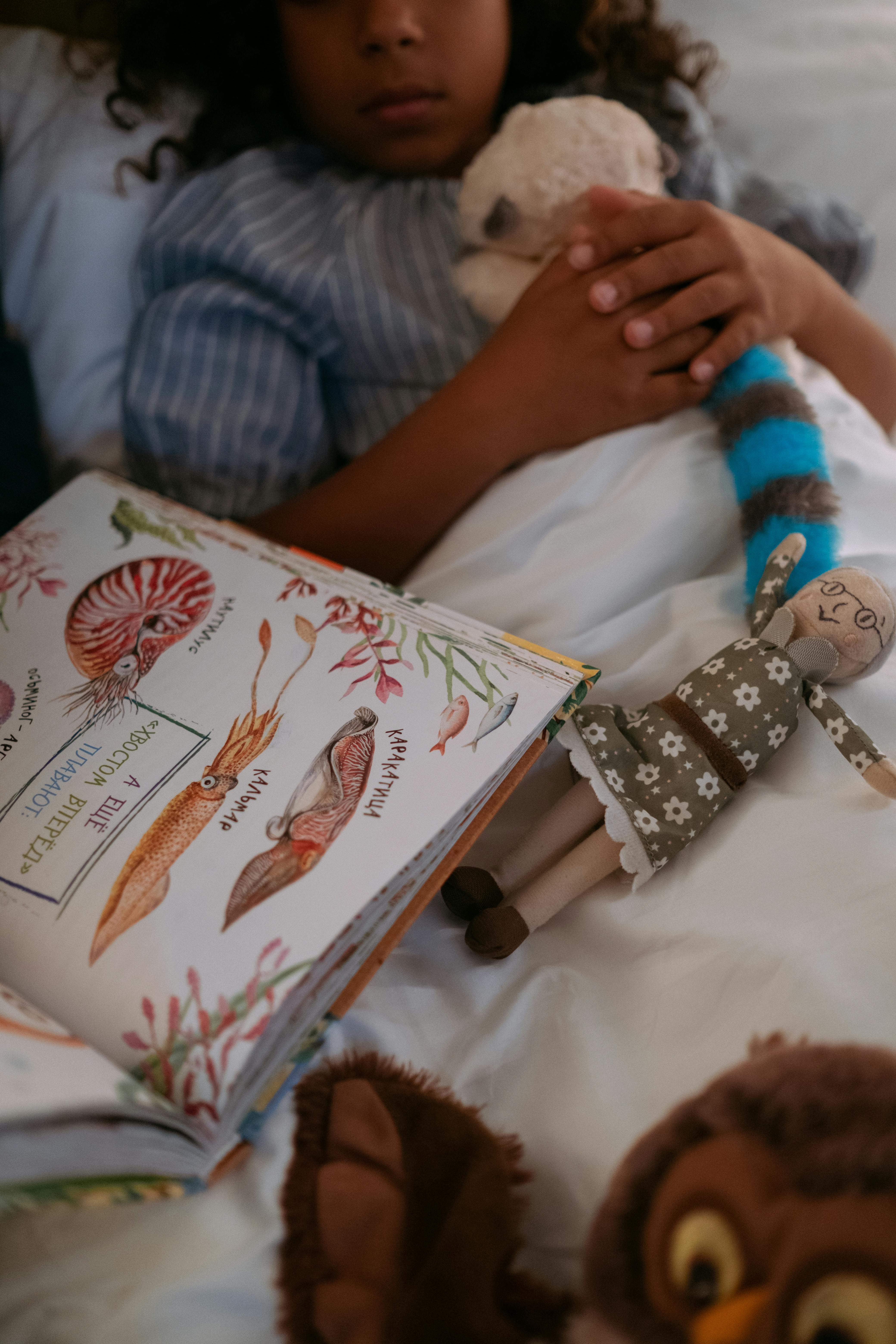 a girl lying in bed beside a book holding her toys