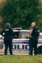 Back view of unrecognizable policewoman with male partner in uniform standing on meadow against automobile and tree