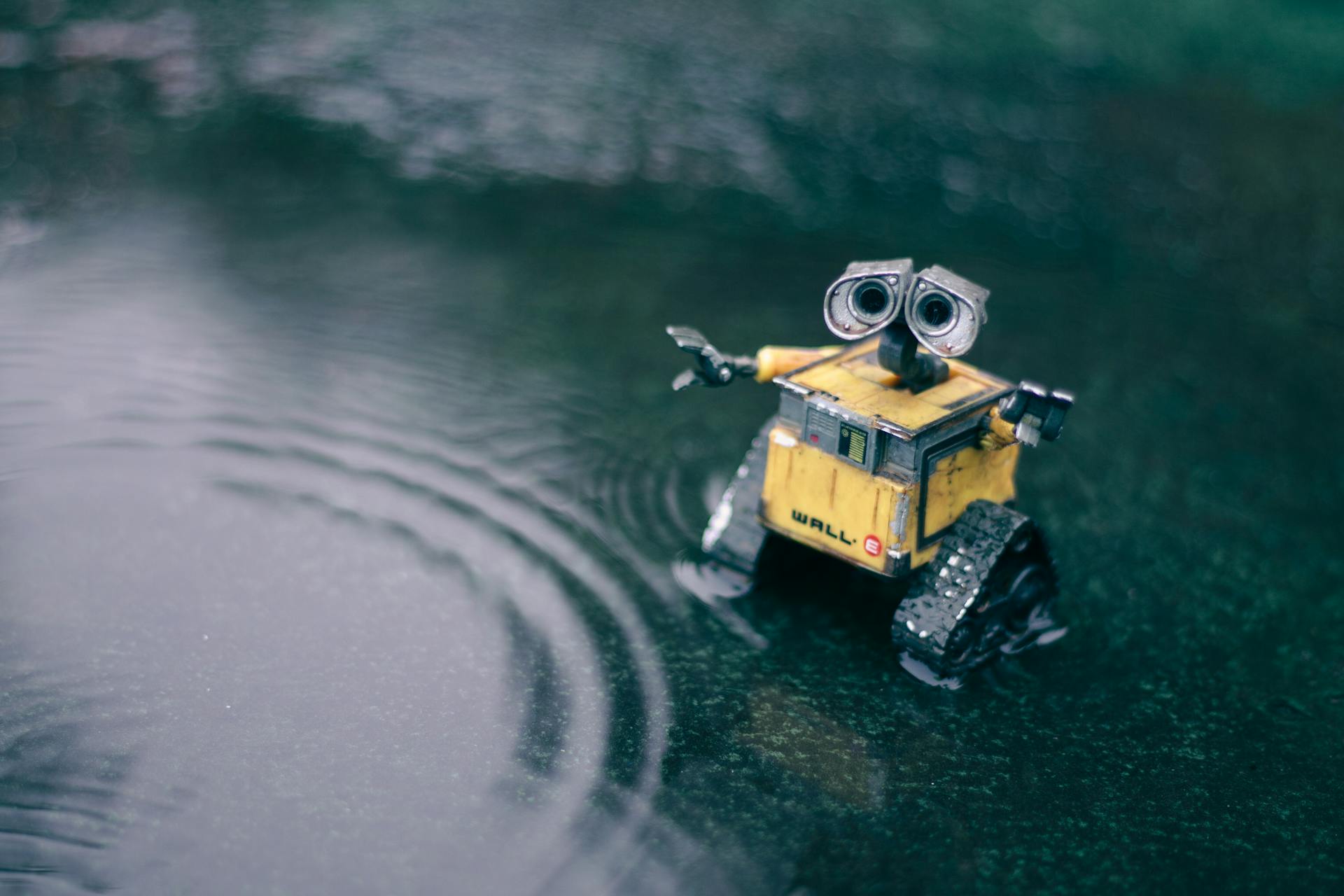 Toy robot in puddle with ripples in daylight