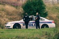 Unrecognizable police officers speaking against car on meadow