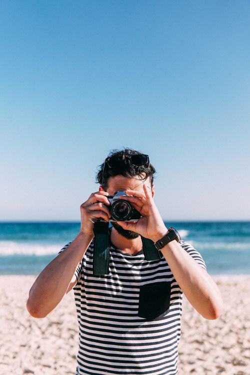 Free Man taking photos on a beach with a DSLR camera under a clear blue sky. Stock Photo