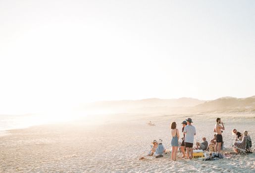 A group of young adults enjoying a sunny day at the beach, surrounded by sand and sea.